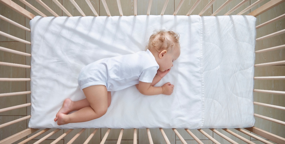 Sweet baby sleeps in his crib on a white sheet without drawings