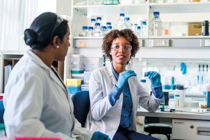 Woman in lab coat gesturing to a collague