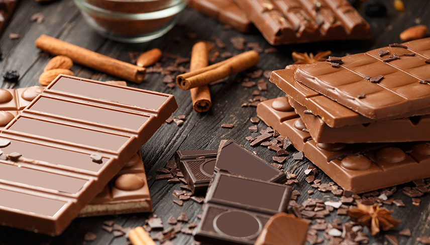 Multiple chocolate bars, chocolate pieces and cinnamon sticks on a dark table